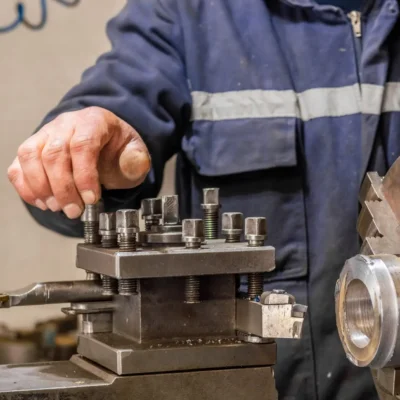 Blue-collar machine operator working with lathe machine in a factory.